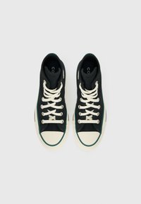 Sneakers de cano alto em tecido preto, com atacadores brancos, biqueira de borracha e realces verdes ao longo da sola. Tecido texturizado e design aerodinâmico.