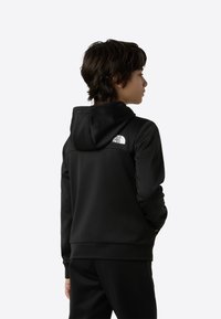 Čierna mikina s kapucňou z mäkkej látky, má kapucňu a logo na chrbte, s rebrovanými manžetami a lemom, v kombinácii s čiernymi nohavicami.