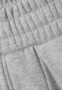 Gros plan sur un tissu gris montrant une ceinture élastique et des coutures de poche latérale sur un vêtement doux, tricoté.