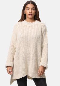 Kremowy sweter z dzianiny z wysokim prążkowanym kołnierzem, długimi rękawami i luźnym krojem. Charakteryzuje się teksturowaną tkaniną i podwiniętymi mankietami.