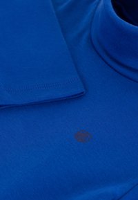 Blå turtleneck skjorte laget av bomull, med en glatt tekstur og en subtil logo på brystet. Mansjetter og krage er ribbestrikket.