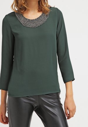 Blusa verde scuro con maniche a tre quarti, colletto rotondo decorato con perline nere e argentate, tessuto morbido e vestibilità comoda.