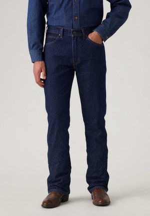 Denim jeans met een diepblauwe kleur, slim fit, vijf zakken, gestikte accenten en een middelhoge taille, aangevuld met bruine laarzen.