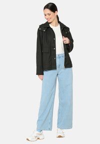 Juoda vandeniui atspari striukė su kapuce, priekinėmis kišenėmis ir auksinėmis detalėmis, derinama su šviesiai mėlynomis plačiomis kelnėmis ir baltais sportbačiais.