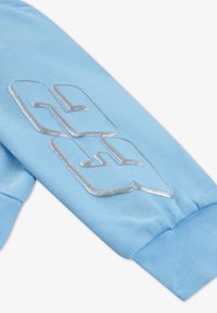 Mingea de sudare de culoare albastră deschisă, cu mânecă, având un logo brodat în argint, cu tipografie modernă. Textură netedă, manșetă ribbed și un design simplu.
