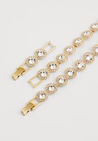 Armband in Goldton mit mehreren kreisförmigen Gliedern, die große klare Strasssteine umgeben von kleineren Kristallen, abgerundet mit einem eleganten Verschluss.
