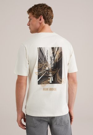 Cream cotton T-shirt featuring a black and gold graphic print on the back, depicting an urban scene with "BLUE RIDGE" text below.