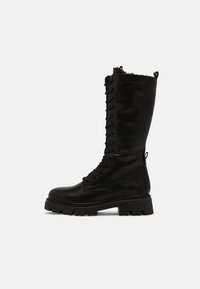 Botas de cuero negras hasta la rodilla con cordones en la parte delantera, suela de goma y acentos texturizados, que presentan un forro suave en la parte superior.