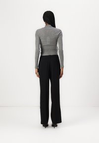 Chemise à col roulé gris à manches longues et pantalon noir taille haute avec une coupe droite. Texture lisse, design minimal et sans motifs visibles.