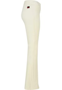 Cream-colored pants with a fitted design, elastic waistband, and a small black and red logo tag on the back. Smooth texture and straight leg.