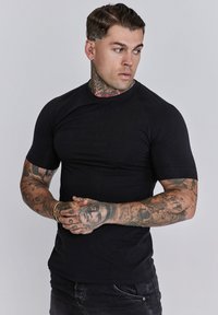 Fekete, testhez simuló póló, rugalmas anyagból, rövid ujjal és kerek nyakkivágással. Finom logó a mellkason.