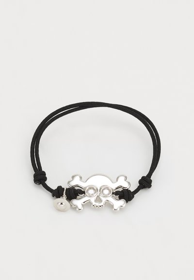 Brățară din fir negru cu un pandantiv în formă de craniu și oase încrucișate din metal argintiu, având două pietre transparente pentru ochi și un închizător rotund din metal.