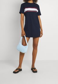 Granatowa sukienka t-shirtowa w czerwone i białe poziome paski, zestawiona z jasnoniebieską torebką i czarnymi klapkami z grubą podeszwą.