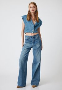 Denimowy outfit składający się z krótkiej, bezrękawnikowej koszuli na guziki oraz spodni typu wide-leg w jasnoniebieskim odcieniu, o gładkiej fakturze i minimalnych detalach.