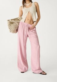 Pantalons larges légers et roses en tissu texturé, associés à un débardeur beige à côtes et un sac tissé aux tons neutres.