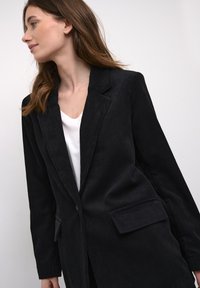 Blazer de pana negra con solapas de muesca, cierre de un solo botón, dos bolsillos frontales, forma estructurada y textura de ribete vertical.