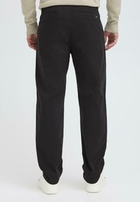 Black cotton pants with a relaxed fit, featuring two back pockets and visible stitching details, paired with white sneakers.