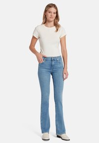 Jeans a zampa d'elefante blu chiaro con vita alta, realizzati in denim, abbinati a una t-shirt aderente a maniche corte color avorio.