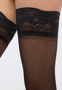 Czarne pończochy do uda z koronkową górą, posiadające przezroczystą teksturę, kwiatowe zdobienia z koronki u góry oraz gładką, nieprzezroczystą część na nogach.