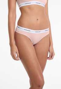 Lichtroze katoenen boxershort met een witte tailleband waarop het logo "GUESS JEANS" staat. Ontworpen voor een strakke fit met minimale bedekking.