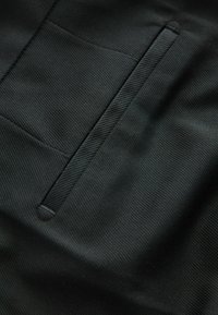 Schwarzer Stoff mit einer feinen gerippten Textur, ausgestattet mit einer Einschubtasche und einer glatten Oberfläche. Das Design ist minimalistisch und modern.