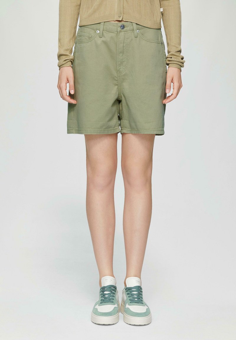 Shorts en coton vert clair avec une coupe décontractée, passants de ceinture et poches avant ; associés à des baskets multicolores avec un design texturé.