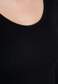 Schwarzes, geripptes Oberteil mit Rundhalsausschnitt. Der Stoff ist glatt mit einem figurbetonten, dehnbaren Design und subtiler Textur.
