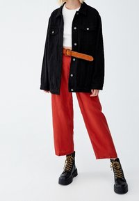 Schwarze Denimjacke mit zwei aufgesetzten Taschen, weißem Oberteil, roten weiten Hosen und schwarzen Kampfstiefeln mit gelben Schnürsenkeln.