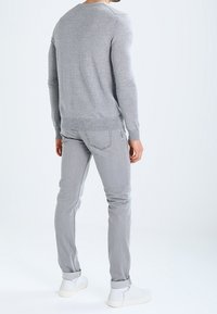 Pull en maille grise, coupe ajustée, encolure ronde. Associé à un jean gris clair et des baskets blanches. Design simple avec des accents minimaux.