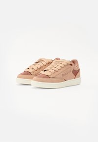 Sneakers Reebok in morbido suede rosa e pelle. Punta arrotondata, collo imbottito e suola in gomma beige. Design con lacci e dettagli del marchio.