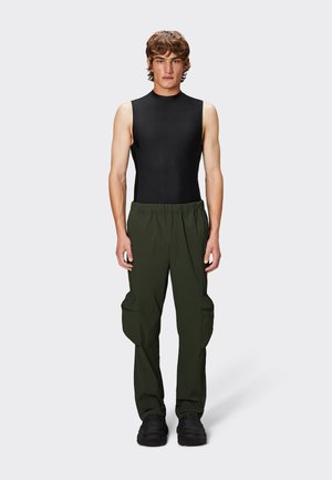 Haut sans manches noir associé à un pantalon cargo ample vert olive avec poches latérales zippées et une taille élastique. Chaussures noires.