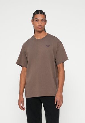 Tricou din bumbac maro cu guler rotund și mâneci scurte, având un mic logo întunecat tonal pe pieptul stâng. Purtați cu pantaloni negri.