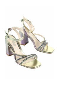 Zelta tonī augstpapēžu sandales ar kvadrātveida purngaliem, dubultām potīšu siksniņām un dekoratīvām rhinestone akcentiem uz krustotajām siksniņām.