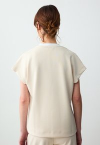 Crèmekleurig top met een zachte textuur, korte mouwen en een ronde halslijn. Naaddetails en een lichte, losse pasvorm.