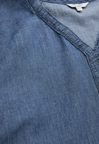 Denim top met een V-hals en contraststiksels. De stof is zacht, in een donkerblauwe kleur met een lichtjes gestructureerde afwerking.