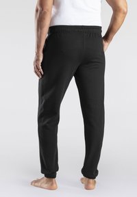 Pantalons de survêtement noirs avec une taille élastique et des poignets de jambes fuselés. Tissu doux avec une texture lisse, adapté à une tenue décontractée.