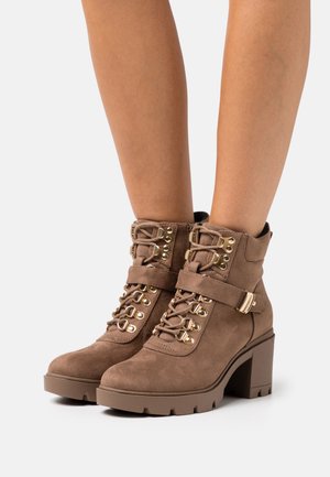 Bottines en daim marron avec un talon bloc chunky. Comprend un devant lacé, des œillets en métal et une sangle décorative avec une boucle dorée.