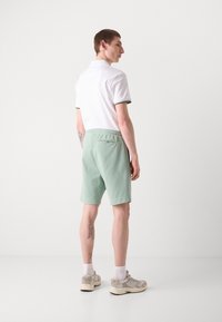 Polo blanc avec des bordures vertes et un short vert clair. Le short possède une taille élastique et une poche arrière. Des baskets sont visibles aux pieds.