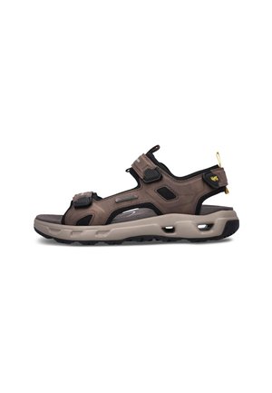 Brune og sorte åbne sportssandaler med tyk beige sål og justerbare velcroremme på hvid baggrund.