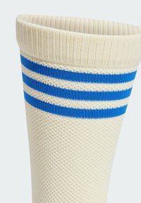 Hvide sokker med tekstureret strik og tre blå striber omkring ribbenet. Designet er simpelt og atletisk, hvilket fremhæver det åndbare materiale.