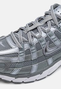 Grauer Sportschuh mit einem Obermaterial aus Mesh, strukturierten Überzügen, einem Schnürsystem und dem markanten Nike-Swoosh. Strukturierte Außensohle mit multidirektionalen Profilen.