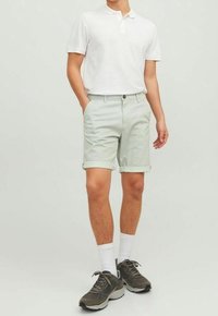 Světlé zelené šortky s strukturovanou tkaninou, s ohrnutými lemy, v kombinaci s bílým polo tričkem a tmavými sportovními botami, nošeny s bílými ponožkami.