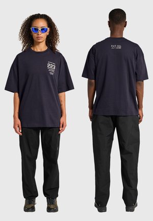 Crew neck, oversized mørkeblå t-shirt med hvid tekstprint på front og ryg, kombineret med sorte løstsiddende bukser og vandresko.