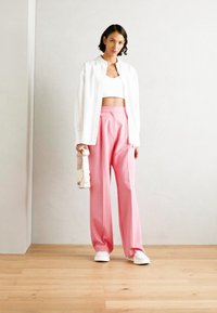 Camisa blanca de botones sobre un top corto blanco, combinada con pantalones de pierna ancha rosa de talle alto y zapatillas blancas. Texturas suaves, diseño minimalista.