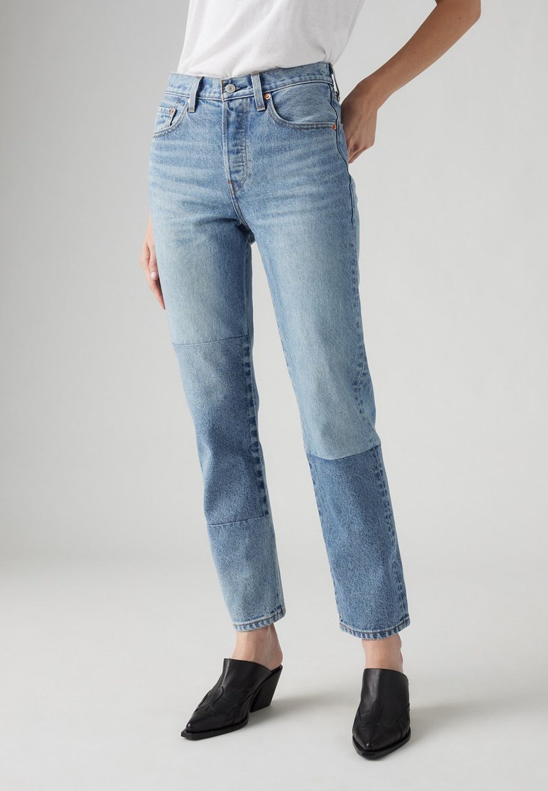Jeans in denim blu chiaro con sfumature variabili, caratterizzati da un taglio dritto, cinque tasche e vita alta. Gli accenti includono cuciture arancioni.