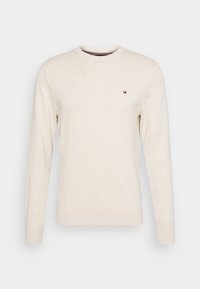 Beige långärmad tröja gjord av mjukt tyg, med rundad halsringning och en liten logotyp på vänster bröst. Slät textur.