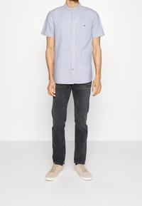 Camisa de rayas con cuello y mangas cortas en azul claro y blanco, hecha de algodón. Se lleva con vaqueros oscuros y zapatillas beige.