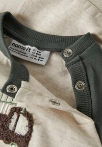 Chemise bébé en coton avec un corps beige et un col côtelé vert foncé, dotée de boutons-pression et d'un détail de broderie en tissu texturé.