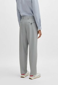 Gray, loose-fitting trousers with a textured finish, featuring a back pocket with a triangular flap and a sleek waistband design.
