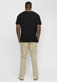 Schwarzes T-Shirt mit kurzen Ärmeln und Rundhalsausschnitt, kombiniert mit hellbeigen Hosen. Der Stoff wirkt weich und hat einen lockeren Schnitt.